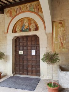 Il portale chiuso della Chiesa di San Fortunato a Montefeltro. Al di sopra, l'affresco di Benozzo Gozzoli